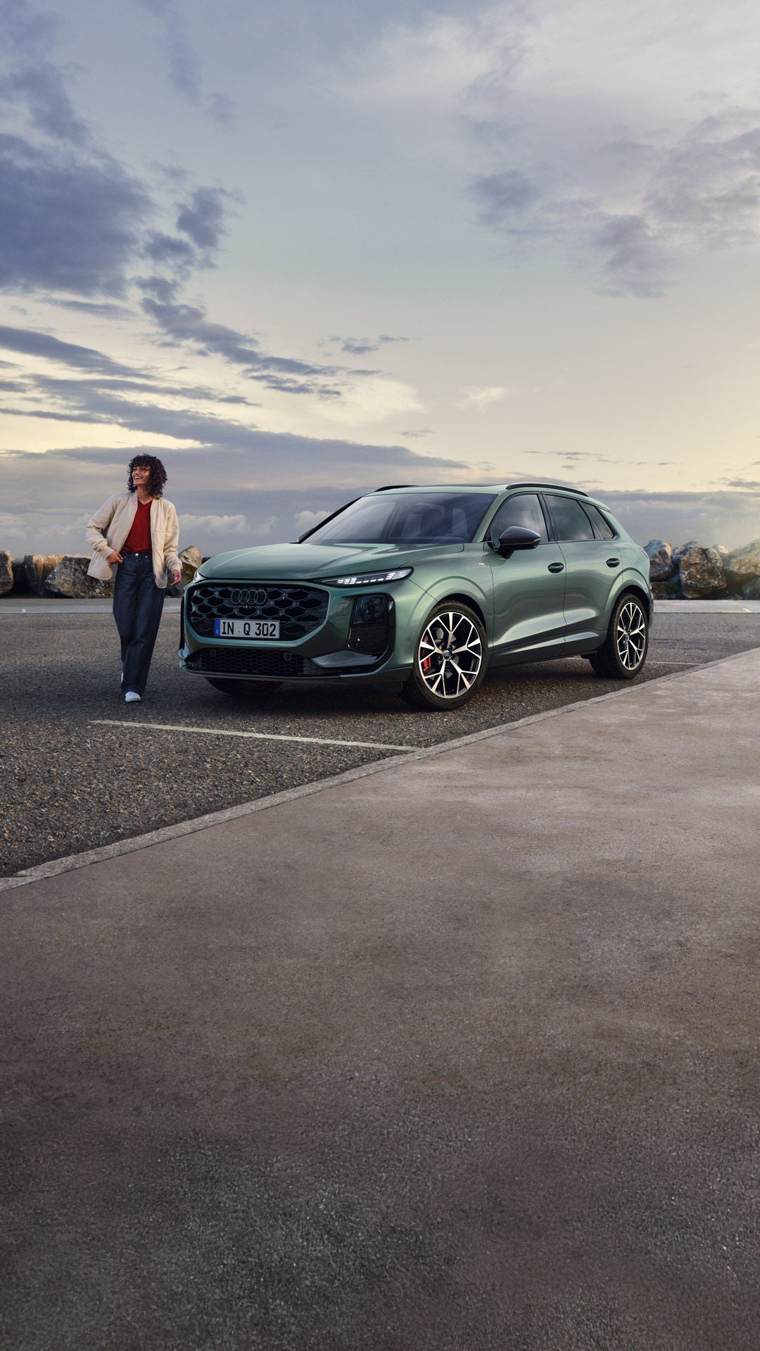 Side view of the parked Q3 SUV on a coastal road, with a young woman standing next to it.