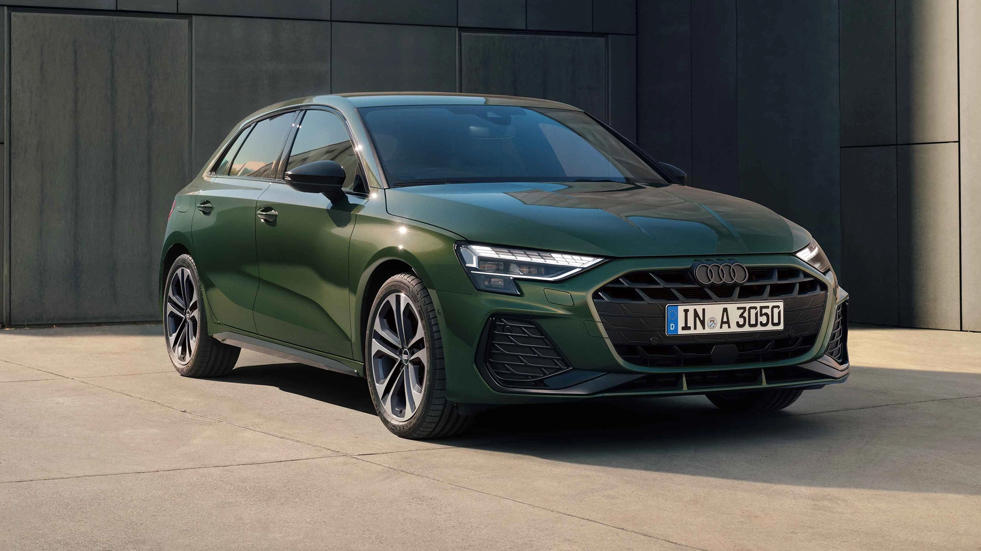 Green Audi A3 Sportback on concrete, facing right. Black grill, silver Audi logo, and white license plate.