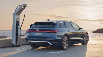 Der S6 Avant e-tron steht seitlich auf einem Parkplatz und ist dabei an eine Ladestation angeschlossen. Hinter dem Parkplatz sind das Meer und Felsen zu erkennen.