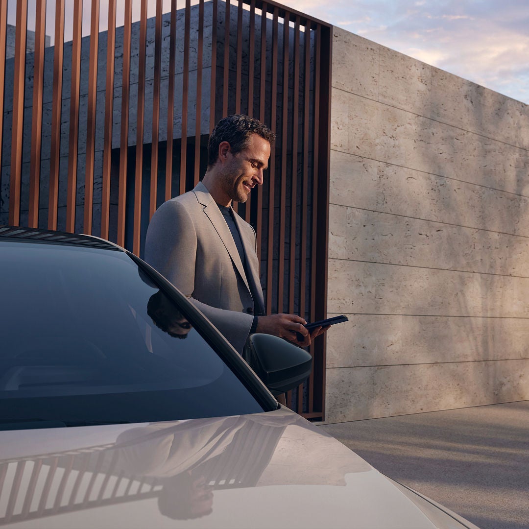 A man dressed in a suit is looking at his smartphone standing next to a white Audi car