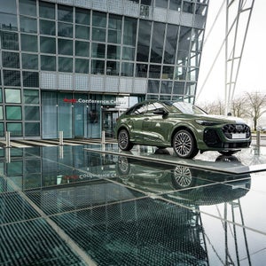 Grüner Audi-SUV vor dem Audi Conference Center mit Glasfassade und Spiegelung im nassen Boden.