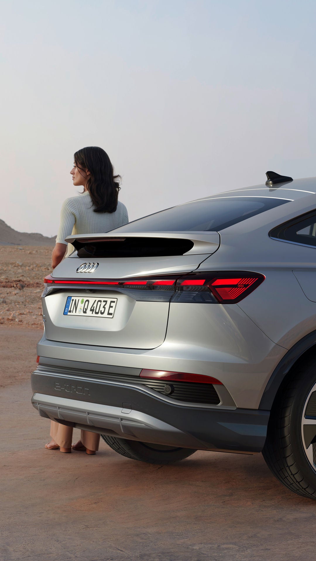 An Audi Q4 Sportback e-tron parked on rugged terrain, a woman is standing beside the rear of the car