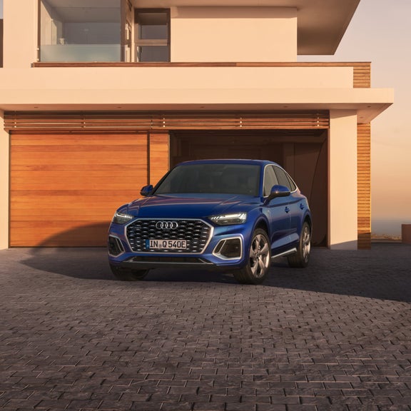 A blue SUV parked in front of a home at sunset.