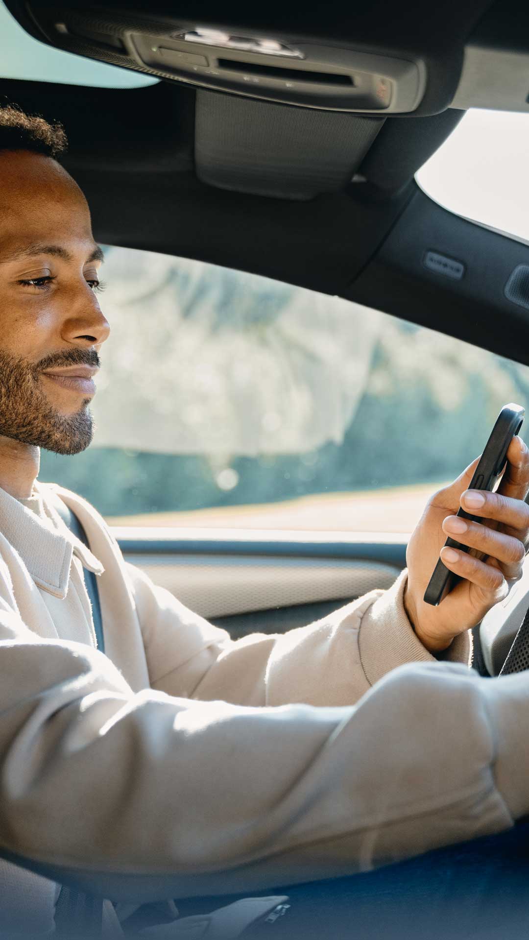 Een man zit in een auto, houdt een smartphone in de ene hand en bedient met de andere hand het touchscreen-display op het dashboard.
