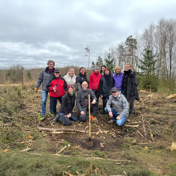 Gruppe von zwölf Personen steht und kniet auf einer aufgeforsteten Lichtung, umgeben von jungen Bäumen und Werkzeugen.