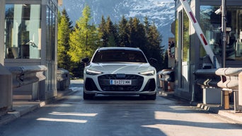Schwarzer Audi fährt bei Schnee durch eine geöffnete Schranke an einer mautpflichtigen Station in den Alpen.
