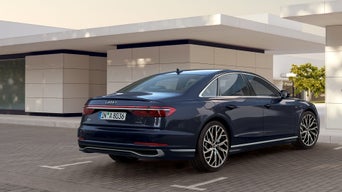 Dunkelblauer Audi A8 parkt vor modernem Gebäude, Heckansicht bei Tageslicht.