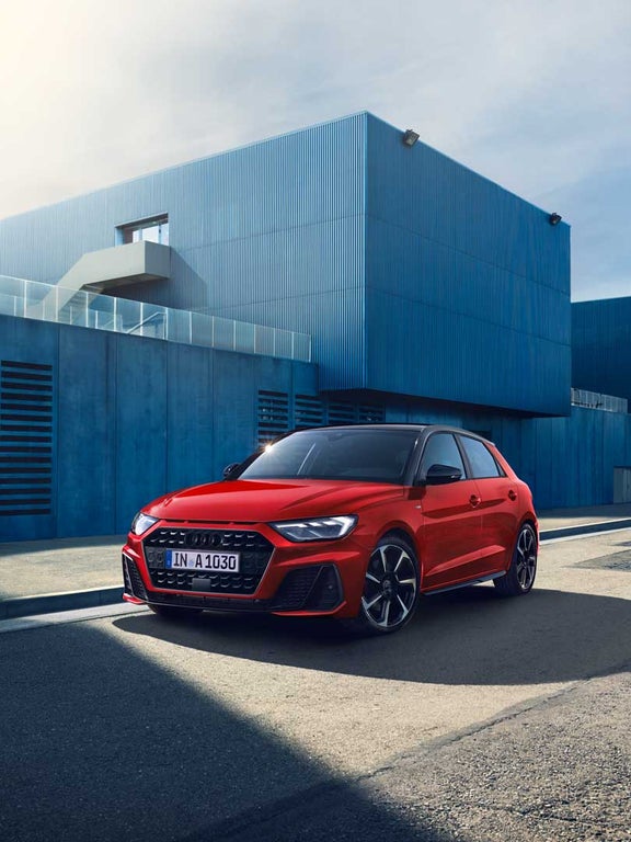 Roter Audi A1 Sportback schräg von vorne links vor einer modernen blauen Metallfassade geparkt.