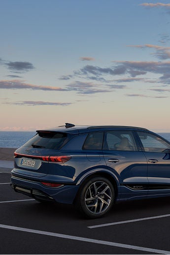 A blue SUV parked by the seaside at dusk, with a person walking in the background.