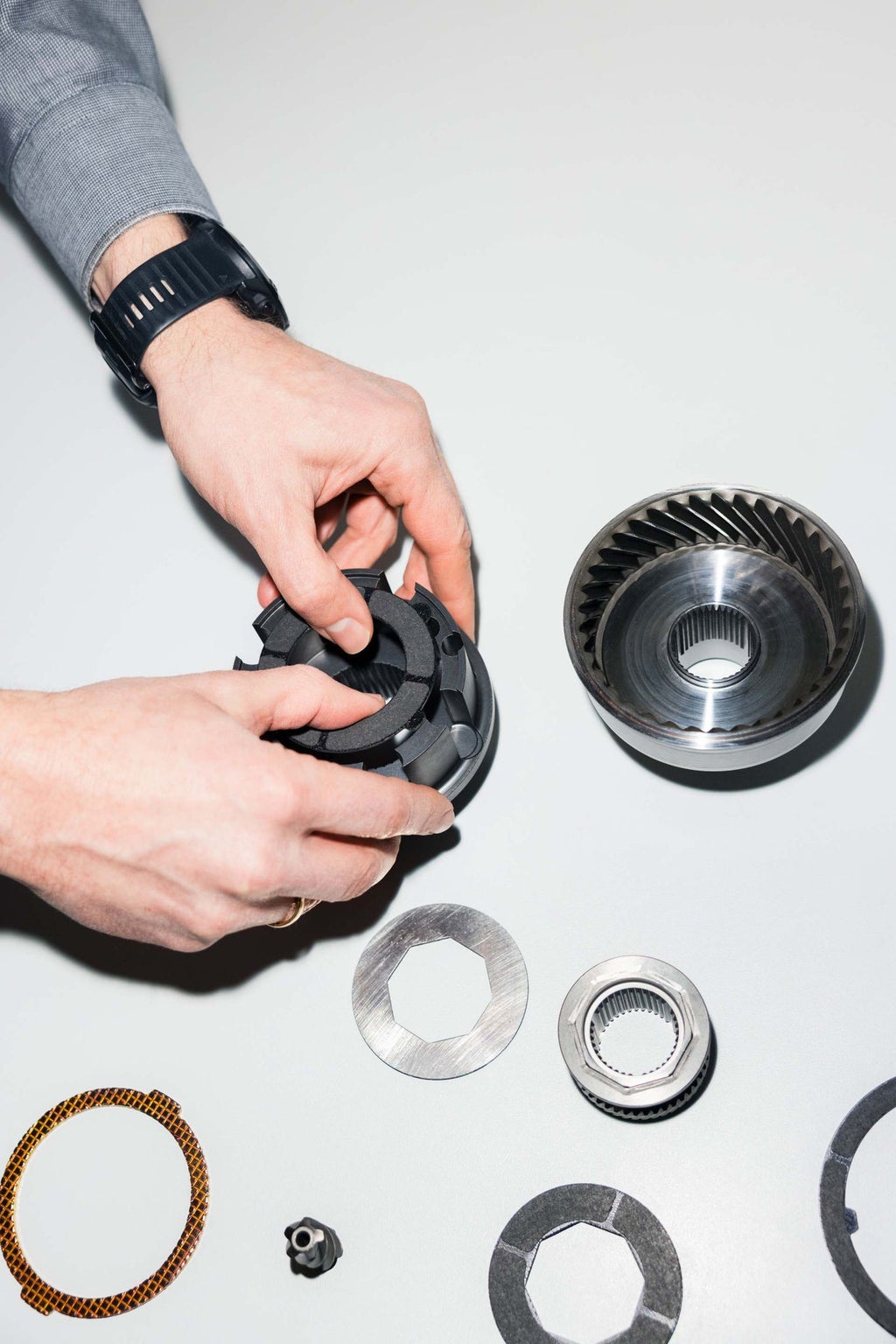 Man sieht die Hände von Dieter Weidemann, wie sie ein Mittendifferenzial in seine Bestandteile zerlegt.
Es liegen insgesamt acht Bauteile auf einem Tisch.