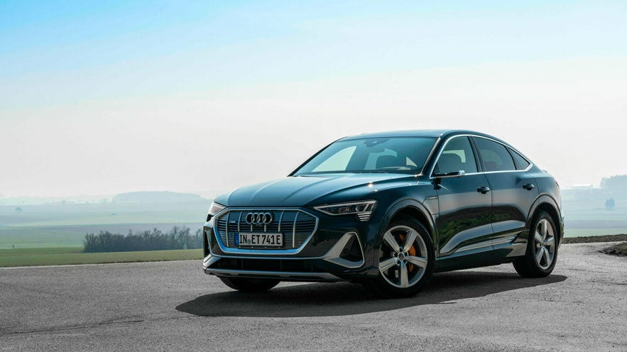 Schwarzer Audi e-tron parkt auf Landstraße bei Tageslicht mit weitem Blick auf Felder und sanfte Hügel im Hintergrund.