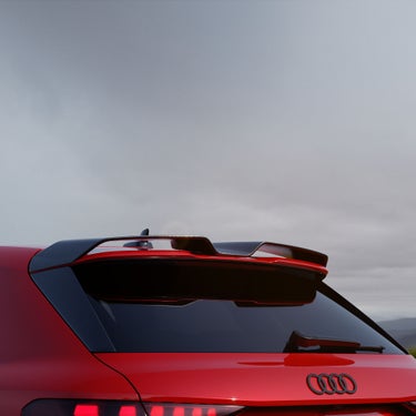 Close-up of a red RS 3 Sportback car's rear with sleek taillights and a sporty spoiler against a cloudy sky, conveying speed and elegance.