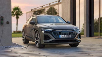 An Audi electric vehicle charging at a home station with palm trees in the background