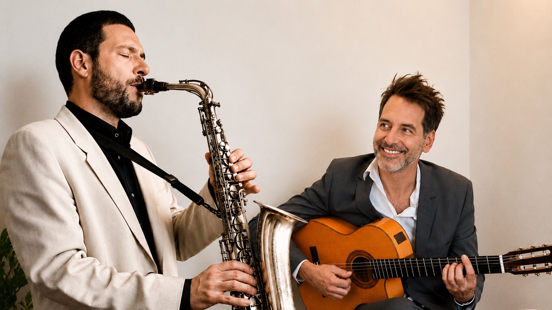 Zwei Männer in Jacketts musizieren: Einer spielt Saxofon, der andere lächelnd eine Konzertgitarre.