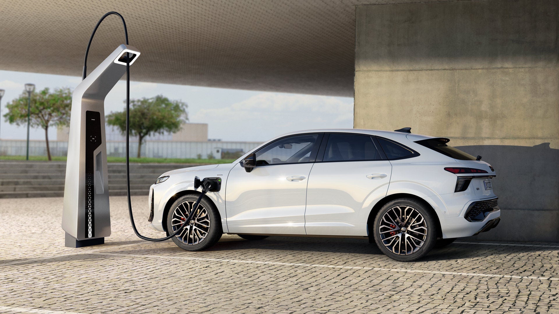 A white Q3 Sportback e-hybrid parked in front of an urban building is charging at a public charging station.	