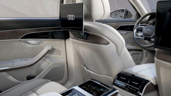 Car interior with modern dashboard, cream leather seats, and Audi logo on screen.