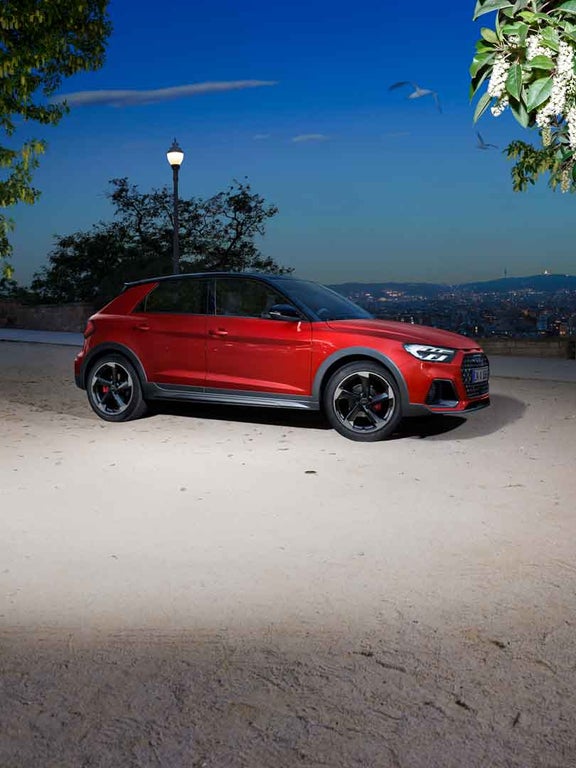 Roter Audi A1 allstreet seitlich aufgenommen bei Nacht mit Stadtpanorama im Hintergrund.