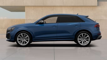Blue Audi RS Q8 SUV parked by a modern beige wall, side view, featuring black windows and silver alloy wheels.