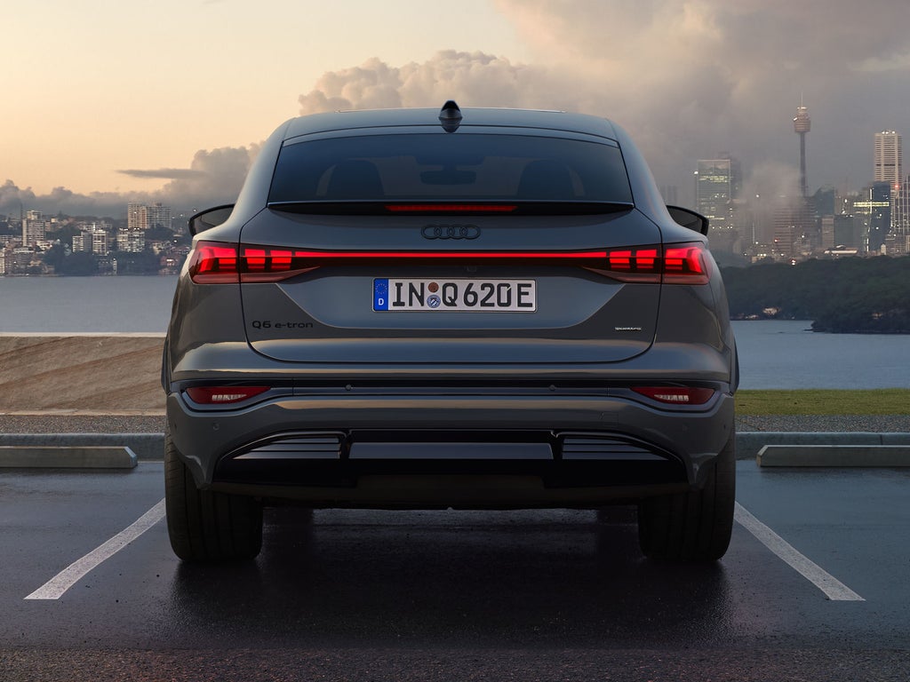 Heckansicht des Q6 Sportback e-tron, welcher auf einem Parkplatz am Meer steht. Im Hintergrund sieht man eine Stadt, welche von Wolken durchzogen ist.