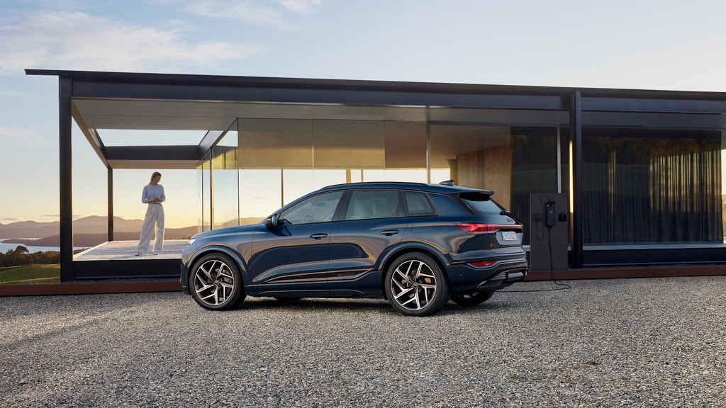 Audi Q6 e-tron set fra siden foran et hus