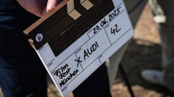 Filmklappe mit handschriftlichem Hinweis „Filmfest München x Audi“ bei einem Außendreh.