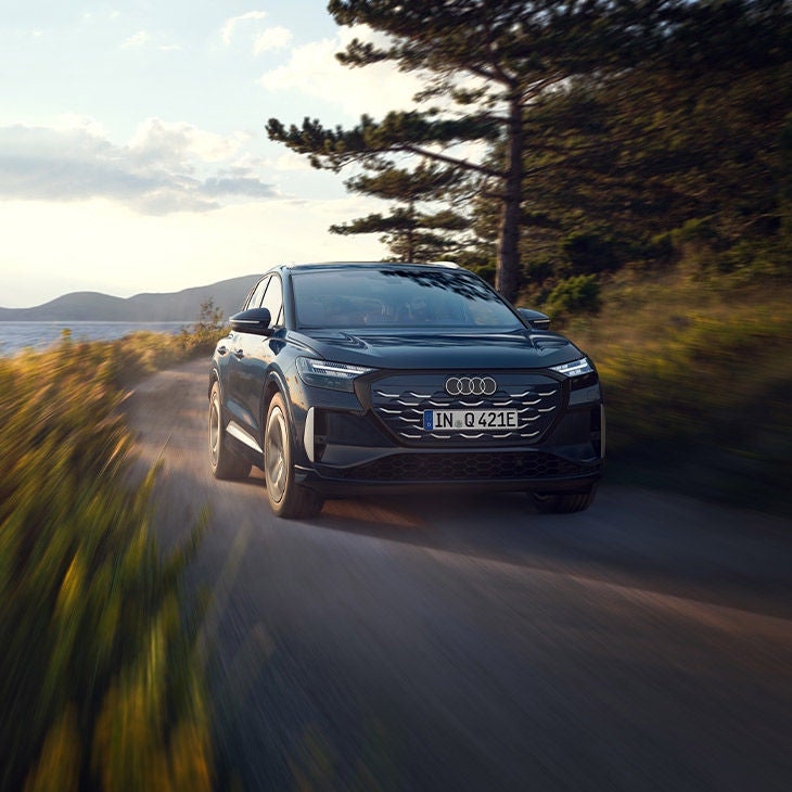 Audi Q4 e-tron noire roulant sur une route de campagne au coucher du soleil.