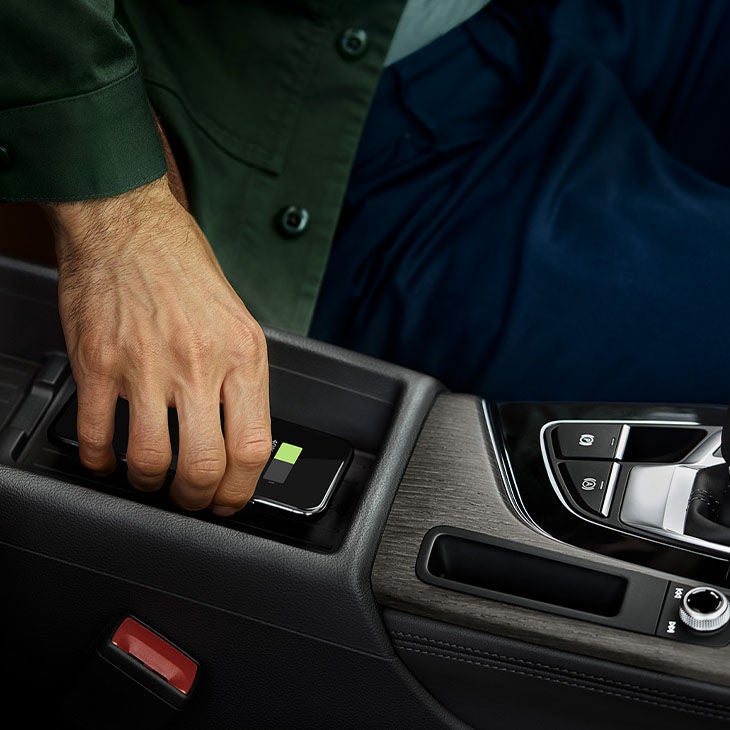 Person placing a smartphone on a car's wireless charging pad.