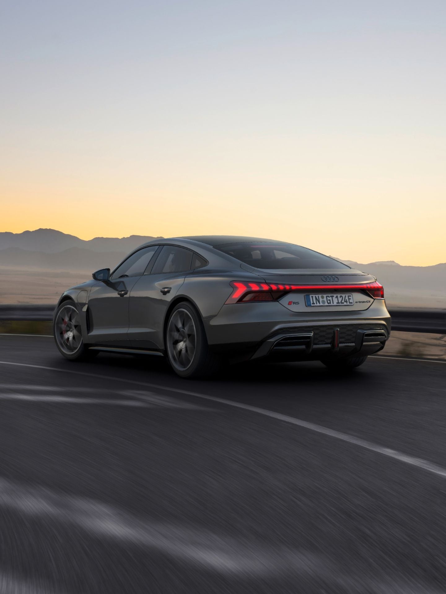 Grey Audi RS e-tron GT driving on highway at dusk with mountainous backdrop.