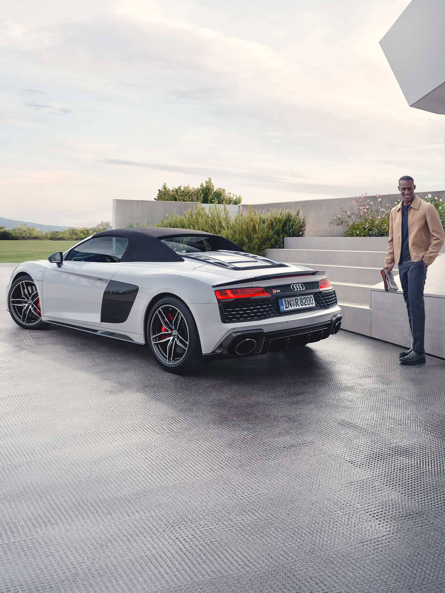 A white metallic Audi R8 convertible parked outside a modern building.