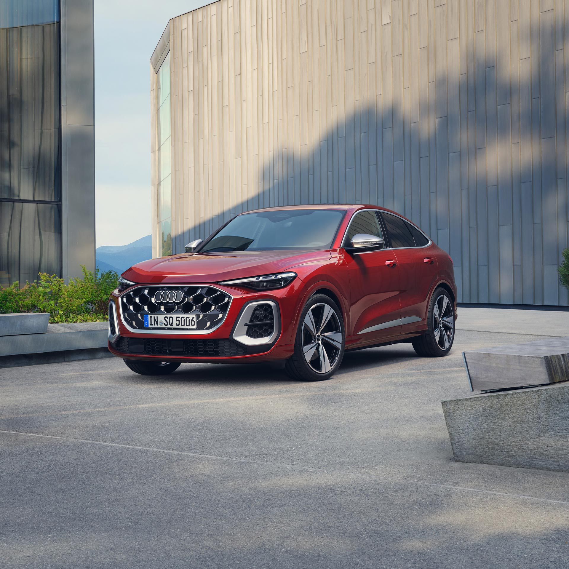 Ein roter Audi SQ5 Sportback steht vor einer modernen Gebäudefassade auf einem hellen Betonplatz.