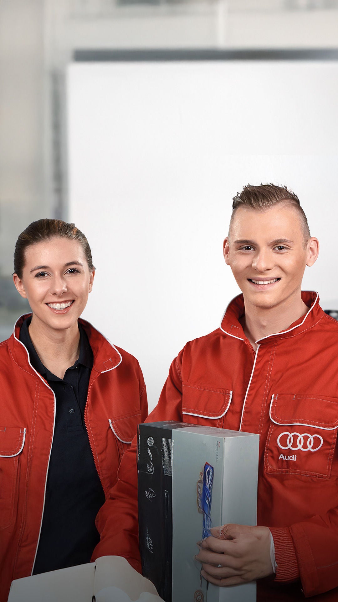 Zwei Auszubildende in roten Jacken mit Audi Logo schauen in die Kamera