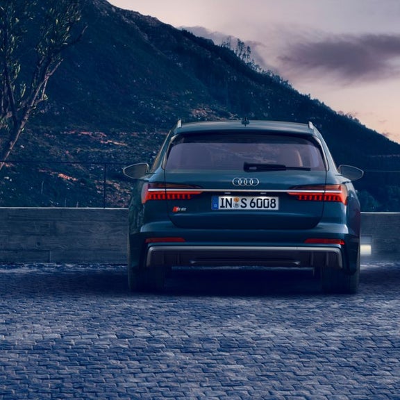 Rear view of a blue Audi S6 Avant car parked before mountain scenery at dusk.
