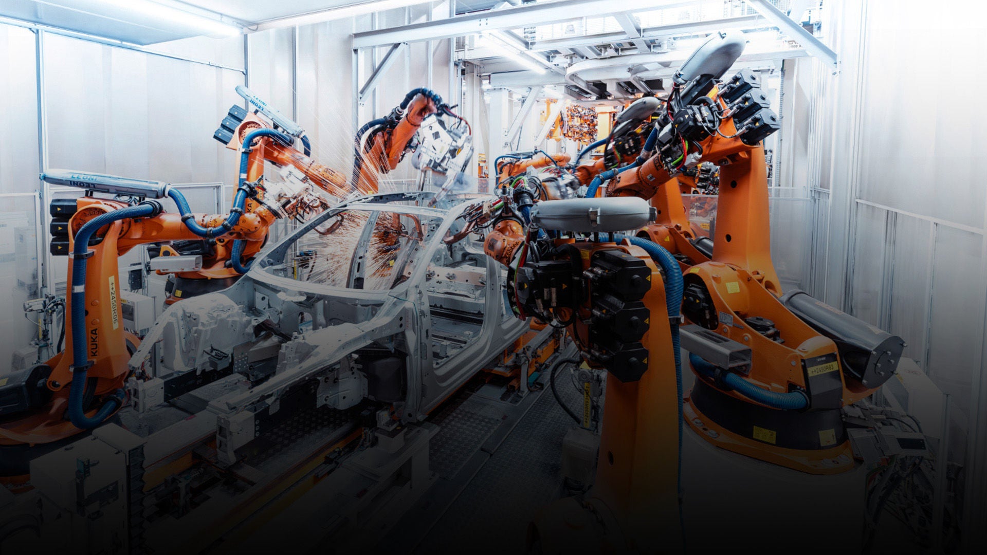 Roboterarme schweißen eine Karosserie in einer hell ausgeleuchteten, automatisierten Fertigungslinie.