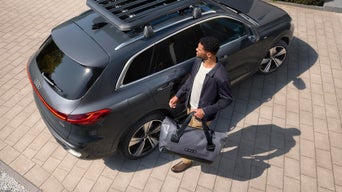 Mann läuft mit der Outdoor-Reisetasche von Audi neben einem Q5 her