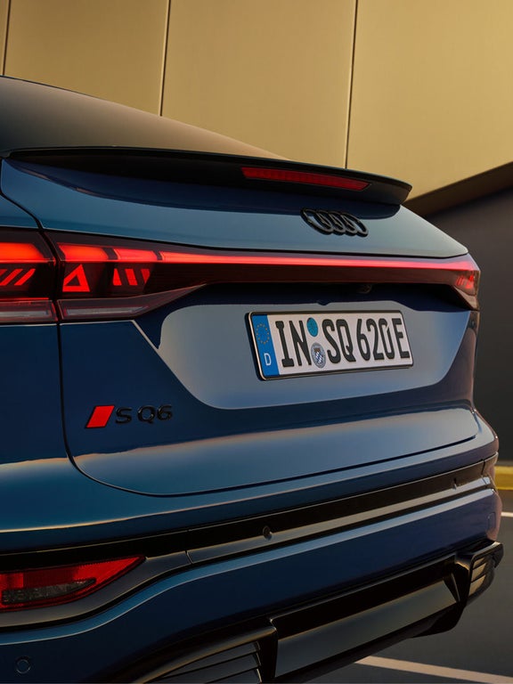 Nahaufnahme des beleuchteten Hecks eines blauen Audi SQ6 Sportback e-tron mit SQ6-Logo und leuchtenden Rücklichtern.