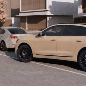 A beige Audi parked beside a white compact car on a modern street, with a contemporary building and autumn trees in the background.