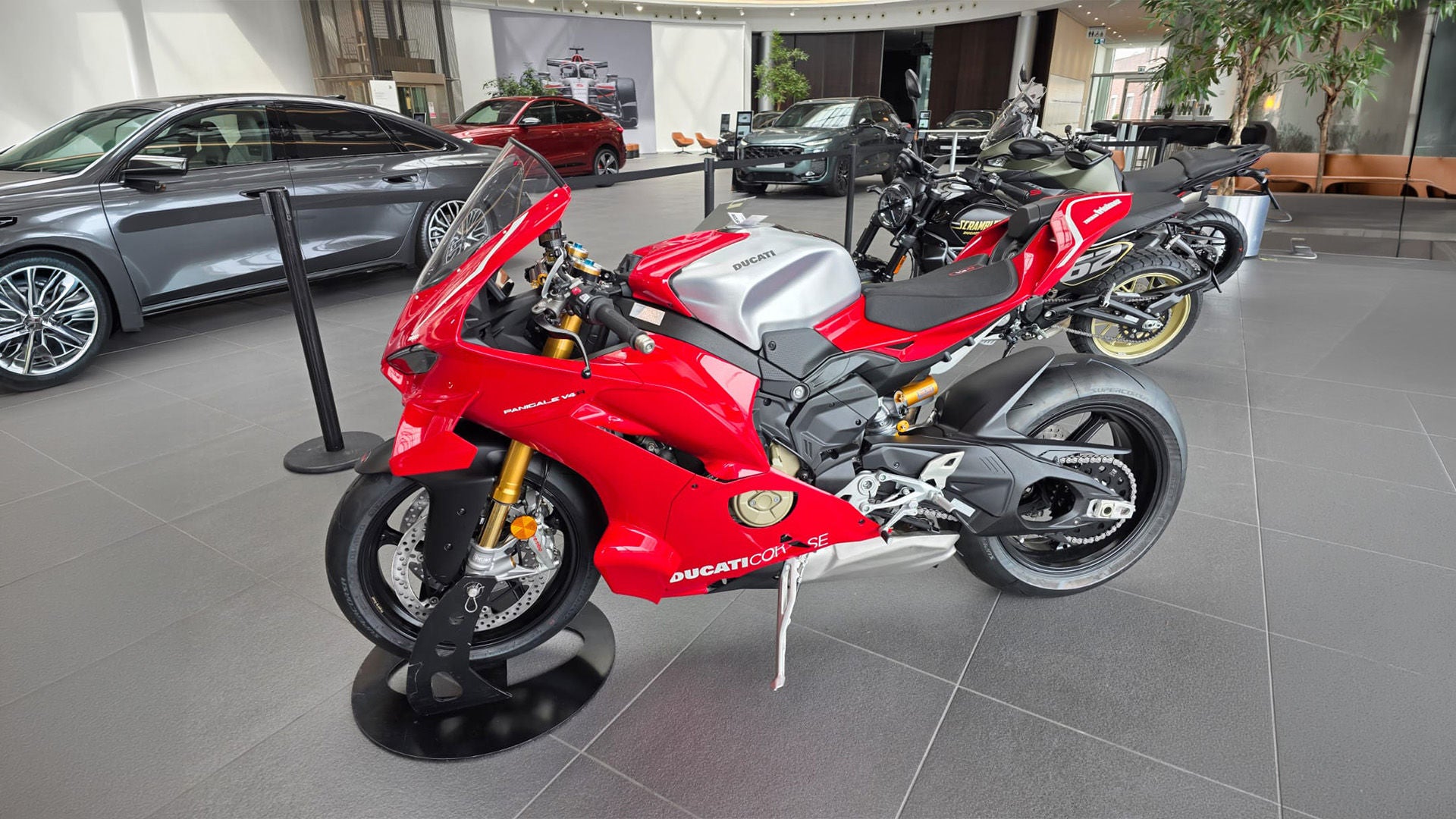 Rotes Ducati-Sportmotorrad im Showroom, umgeben von Autos und weiteren Motorrädern.