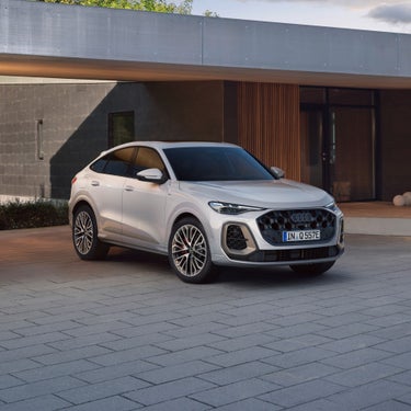 A silver Audi Q5 SUV parked in front of a modern home, showcasing its sporty design and stylish alloy wheels on a stone driveway.