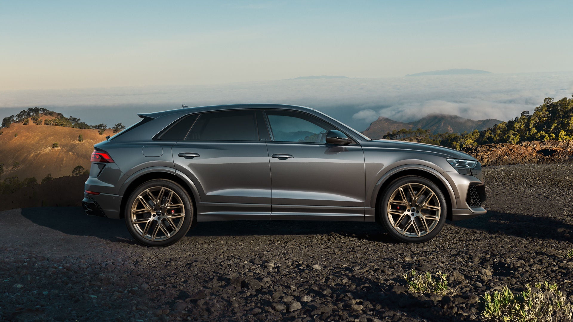 Der RS Q8 SUV in Seitenansicht auf einem Schotterweg, umrahmt von kargen Felsen. Im Hintergrund sind Wolkenbänder zu erkennen.