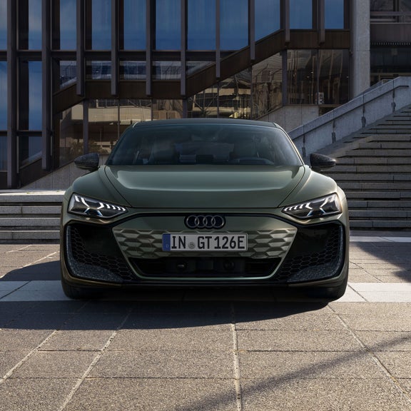 Grüner Audi RS e-tron GT performance frontal vor einem modernen Gebäude mit Treppe und Glasfassade.