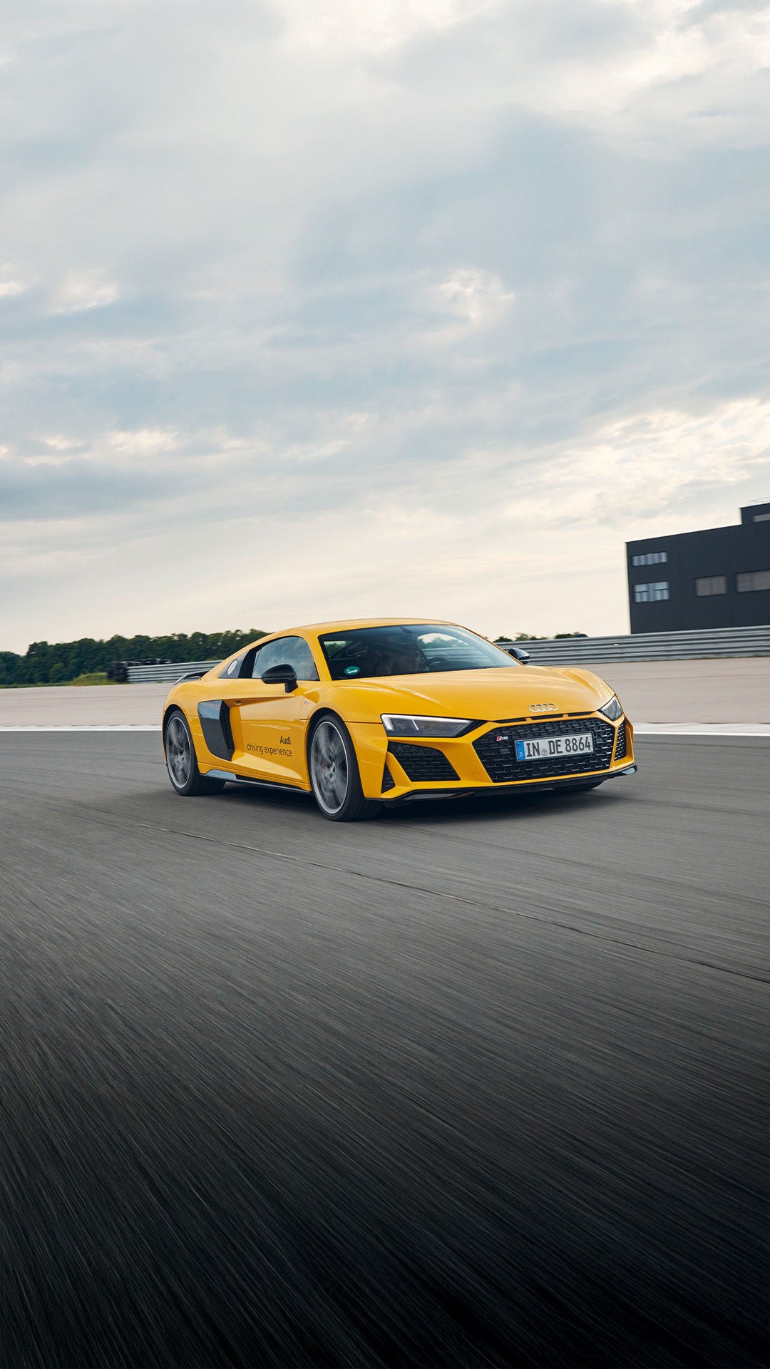 Gelber Audi R8 Coupé V10 performance quattro fährt auf einer breiten Rennstrecke bei bewölktem Himmel.