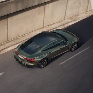 Um Audi RS e-tron GT performance verde é visto de cima e por trás, trafegando em uma rodovia ladeada por altos muros de concreto.