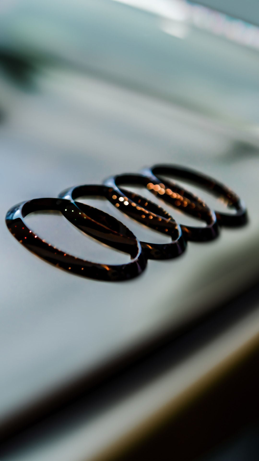 Nahaufnahme des glänzenden Audi-Ringsymbols auf einer Fahrzeugoberfläche mit unscharfem Hintergrund.