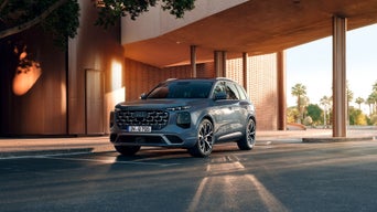 Une Audi Q7 grise garée sous un auvent moderne à l'entrée d'un immeuble.