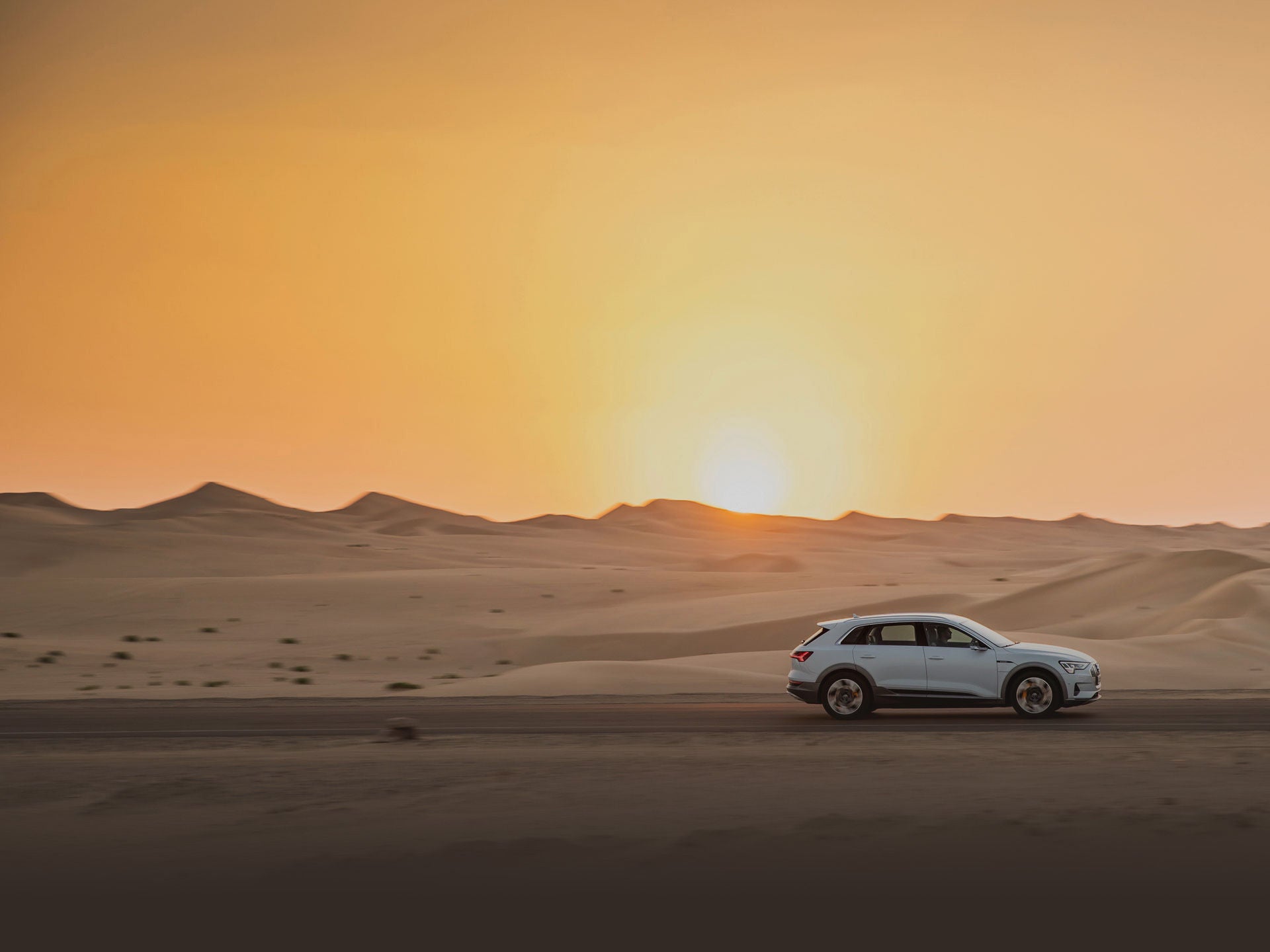 Audi fährt in der Wüste bei Sonnenuntergang