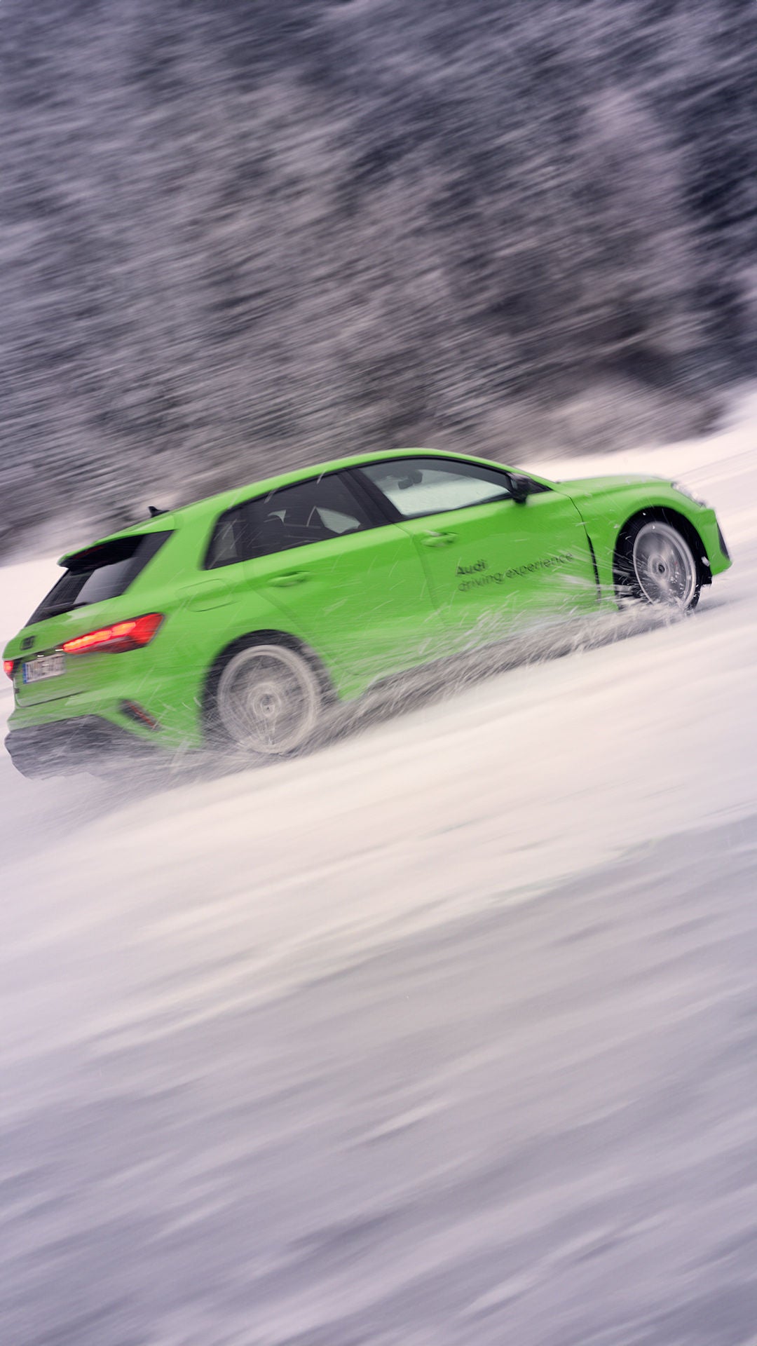 Hellgrüner Audi RS 3 Sportback wirbelt beim Driften im Schnee Wasser und Schnee auf.