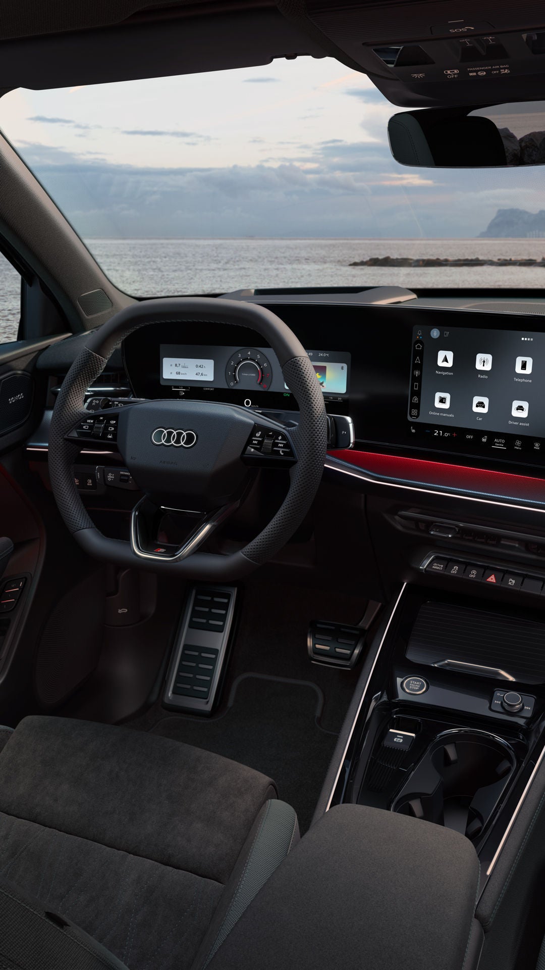 Vue arrière de l'habitacle de l'Audi Q3 SUV, mettant en avant le volant, l'écran panoramique et le pack d'éclairage d'ambiance rouge. On aperçoit la mer à travers le pare-brise.