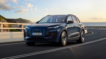Blue Audi Q6 e-tron SUV driving on a curved road with sea at the far back