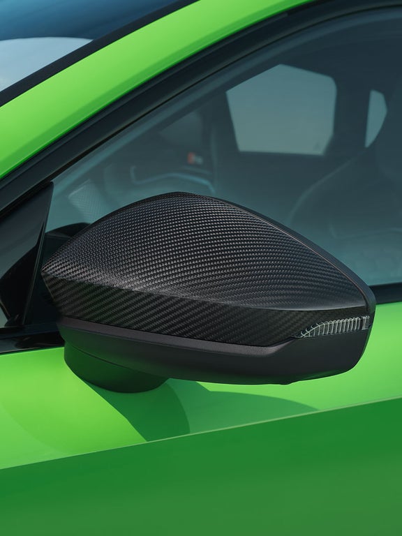 Nahaufnahme eines Außenspiegels mit glänzender Carbonfaser-Oberfläche an einem hellgrünen Audi RS 3 Sportback.