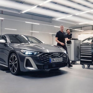 Two technicians in a garage with an Audi car parked